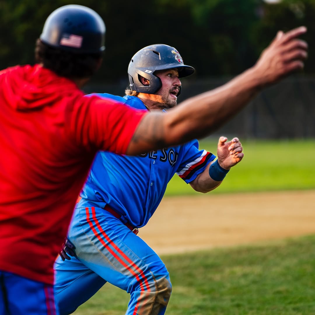 Baseball player in blue uniform sliding into base with another player in red attempting to tag him out.